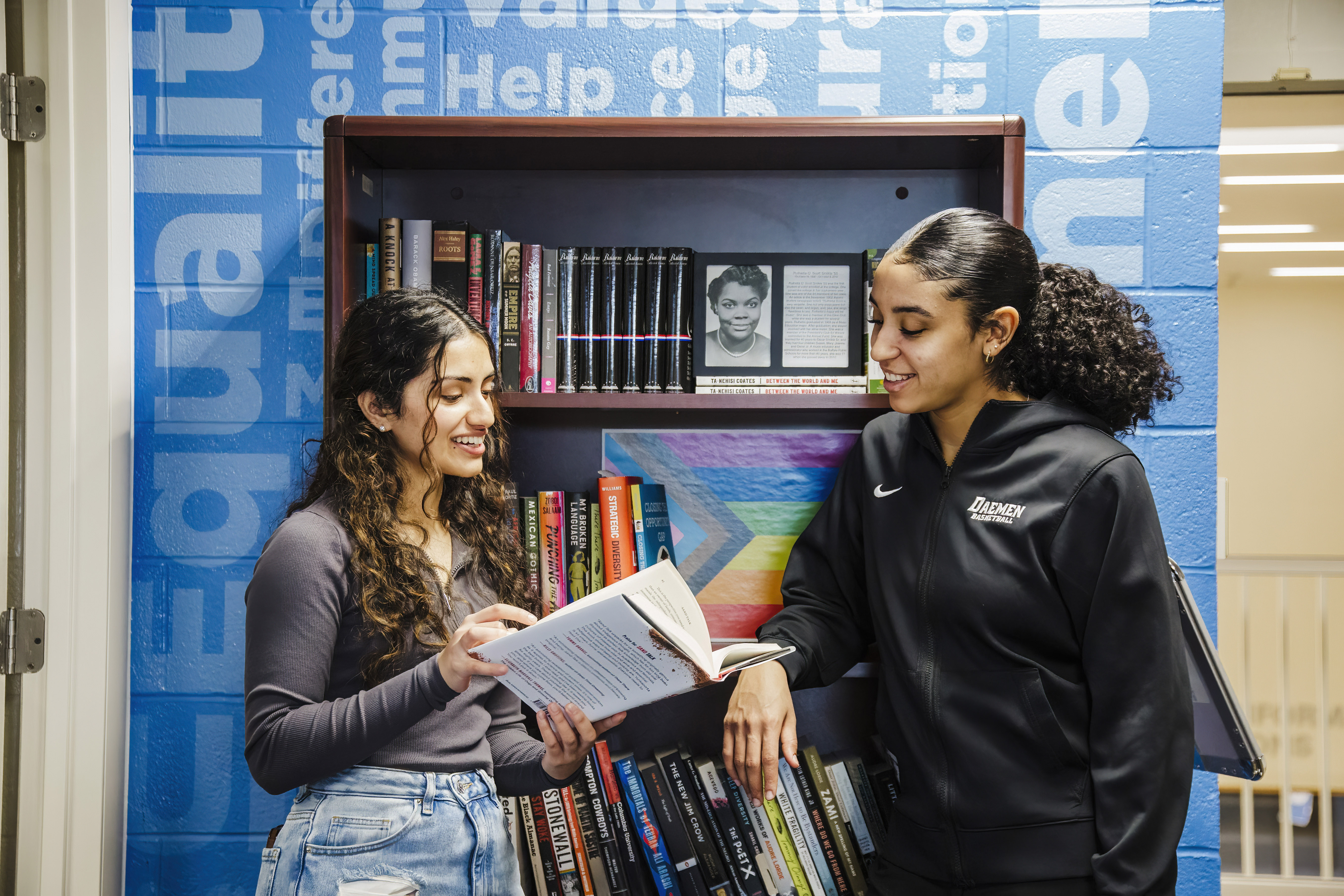 Two students in front of bookcase looking at a diverse book together