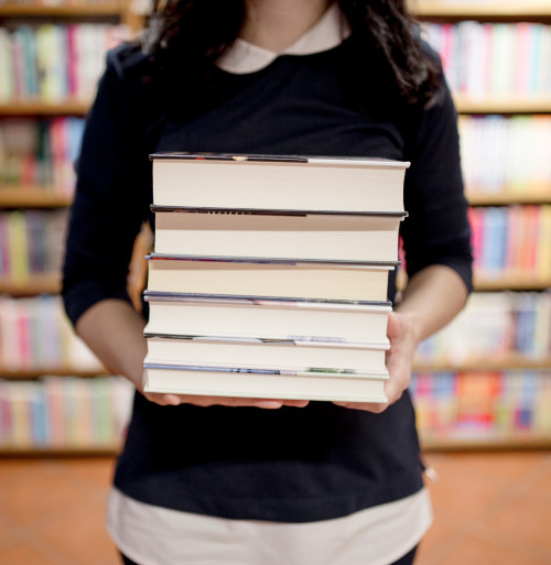 Female holding a stack of books with shelves of books in the distance